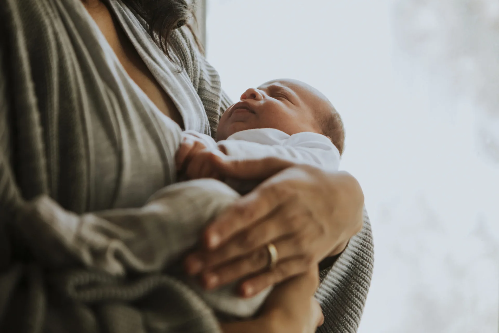 A new mother in a soft gray cardigan cradling her sleeping newborn baby